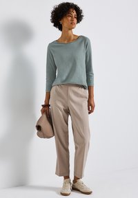 Hellblaues Langarmoberteil, beige maßgeschneiderte Hose, braune Handtasche, cremefarbene Sneakers; zeichnet sich durch eine weiche Textur und eine lockere Passform mit dezenten Mustern aus.