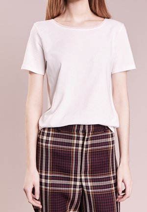 Femme portant un t-shirt blanc uni à manches courtes et un pantalon à carreaux taille haute dans des tons bordeaux, marron et crème.
