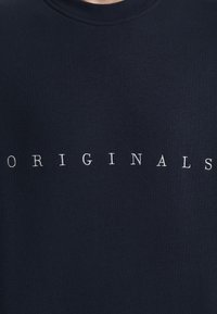 Námořnická modrá mikina vyrobená z bavlny, s žebrovaným výstřihem a bílým nápisem "ORIGINALS" umístěným uprostřed na hrudi.