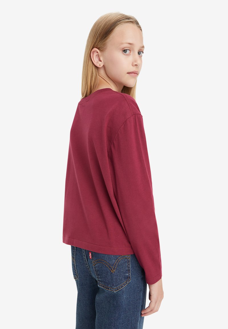 Bordeauxrotes Langarmshirt mit lockerer Passform, Rundhalsausschnitt und weichem Baumwollmaterial. Kombiniert mit blauen Jeans aus Denim mit einem Logo-Label auf der Rückseite.