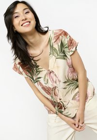 Blusa floreale in tessuto leggero con grandi foglie rosa e verdi, maniche corte, scollatura a V e un nodo in vita.