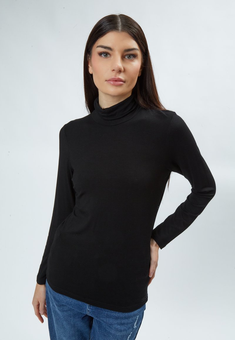 Schwarz langärmliges Turtleneck-Oberteil in figurschmeichlerischem Stil, aus glattem Stoff, kombiniert mit blauen, verwaschenen Jeans. Keine sichtbaren Muster oder Hardware.