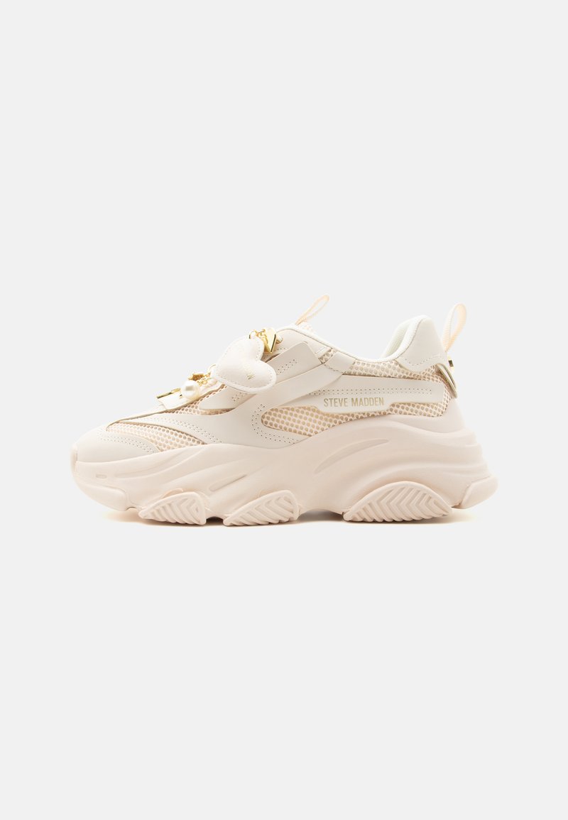 Baskets beige clair épaisses avec panneaux en mesh, semelle épaisse, fermeture éclair dorée, breloque en forme de cœur et marquage « Steve Madden » sur le côté.