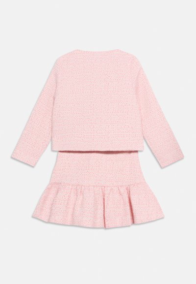 Ροζ μακρυμάνικη μπλούζα με υφή, σε συνδυασμό με φούστα καμπάνα στο ίδιο σχέδιο, αμφότερα με απαλό υφαντό μοτίβο σε λευκό φόντο.