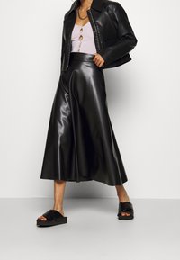 Schwarze Kunstlederjacke mit einem taillierten Design, kombiniert mit einem schwarzen, glänzenden A-Linien-Rock und schwarzen Sling-Pumps. Texturiert, moderner Look.