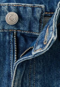 Blauwe spijkerbroek van denim met een zilverkleurige metalen knoop en ritssluiting. Zichtbare stiknaden met een lichte verwering en verstevigde stof bij de knoop.