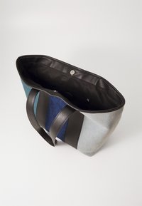 Sac fourre-tout en denim avec des poignées en cuir noir ; présente un design en patchwork dans des teintes bleu clair, bleu foncé et sarcelle ; l'intérieur est doublé de tissu noir.