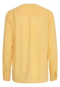 Blusa gialla a maniche lunghe realizzata in tessuto morbido, con una vestibilità rilassata, piega sul retro e polsini abbottonati.