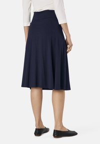 Gonna svasata blu navy con una texture liscia e una vita alta, che termina poco sopra le caviglie, abbinata a scarpe nere basse.