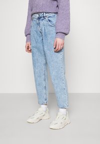 Vaaleansiniset korkeavy ötäröiset farkut, suora lahje, kulutettu tyyli, yhdistetty valkoisiin lenkkareihin ja violettiin teksturoitu neuleeseen.