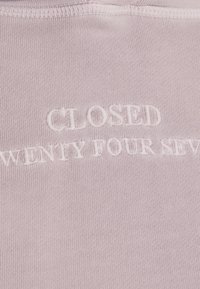 Světle růžová látka s vyšitým textem "UZAVŘENO DVACET ČTYŘI HODINY DENNĚ". Hladká textura, ležérní design s jemnými detaily šití.