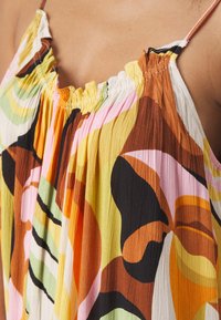 Floral-patterned, pleated top featuring a mix of yellow, pink, green, and brown colors with thin straps and a ruffled neckline.
