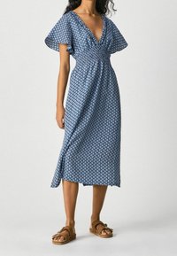 Modré midi šaty s potiskem a krátkými volány, V-výstřihem a zpevněným pasem. Obsahují geometrický bílý vzor na měkké tkanině.