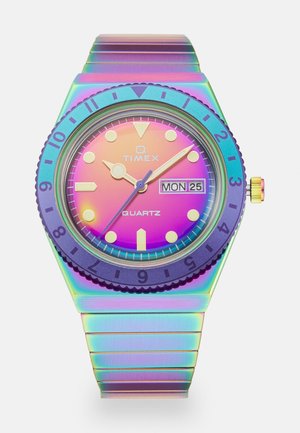 Montre à quartz avec un bracelet en métal irisé. Lunette ronde violette avec des marquages pour les minutes. Cadran dégradé de rose à violet, index des heures dorés et affichage de la date.