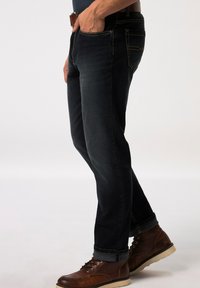 Jeans in denim blu scuro con cuciture a contrasto, vestibilità dritta e orli arrotolati; abbinati a stivali in pelle marrone.