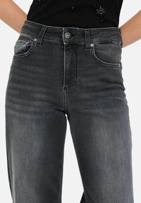 Grijze high-waisted jeans van denim. Kenmerken zijn vijf zakken, een ritssluiting en metalen knoopaccenten. De textuur lijkt licht versleten.