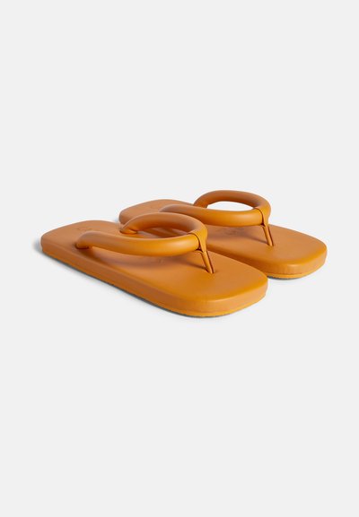 Oranssit kumiset sandaalit, joissa on tasainen pohja ja pyöreä hihna, joka yhdistää varvastuen yläosaan. Sujuva pinta, minimalistinen muotoilu.
