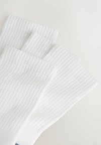 Calzini bianchi a coste caratterizzati da una consistenza morbida. Il design include tre coppie sovrapposte con un motivo delicato e una parte superiore risvoltabile.