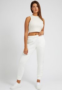 Weißes, kurz geschnittenes Tanktop und passende Jogginghose mit Kordelzugbund, aus geripptem Material und mit Bündchen an den Knöcheln. Kombiniert mit weißen Sneakers.