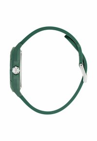 Montre avec un bracelet en silicone vert, un cadran rectangulaire, des garnitures en argent et une finition lisse et texturée, mettant en avant un design minimaliste.