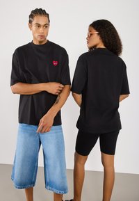 Black short-sleeve t-shirts with a red heart emblem, paired with light blue baggy shorts and black cycling shorts. Smooth cotton fabric texture.