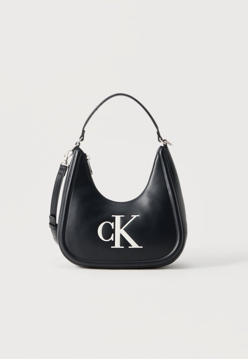 Μαύρο δερμάτινο τσαντάκι ώμου με ασημένιο λογότυπο "cK", καμπυλωτή σιλουέτα, κοντή λαβή και αποσπώμενο μακρύτερο λουρί σε απλό φόντο.