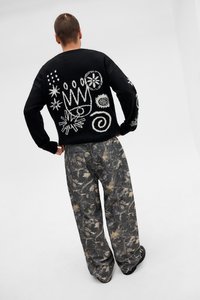 Μαύρο πλεκτό πουλόβερ με λευκά αφηρημένα σχέδια στην πλάτη. Συνδυάζεται με φαρδιά γκρι καμουφλάζ παντελόνια με λεπτό σχέδιο φύλλων.