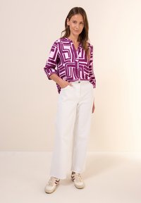 Paarse en roze geometrisch patroonshirt, relaxte pasvorm, knoopsluiting, gecombineerd met witte brede broek en beige sneakers. Zachte textuur.