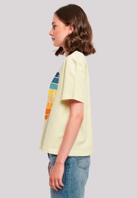 Light yellow cotton t-shirt with short sleeves, featuring a multicolored, retro-inspired graphic design in horizontal stripes.