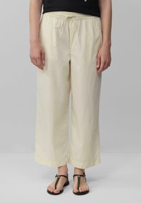 Lichtbeige wijde broek met een elastische tailleband en trekkoord, gemaakt van een soepele, lichte stof. Gecombineerd met zwarte sandalen.