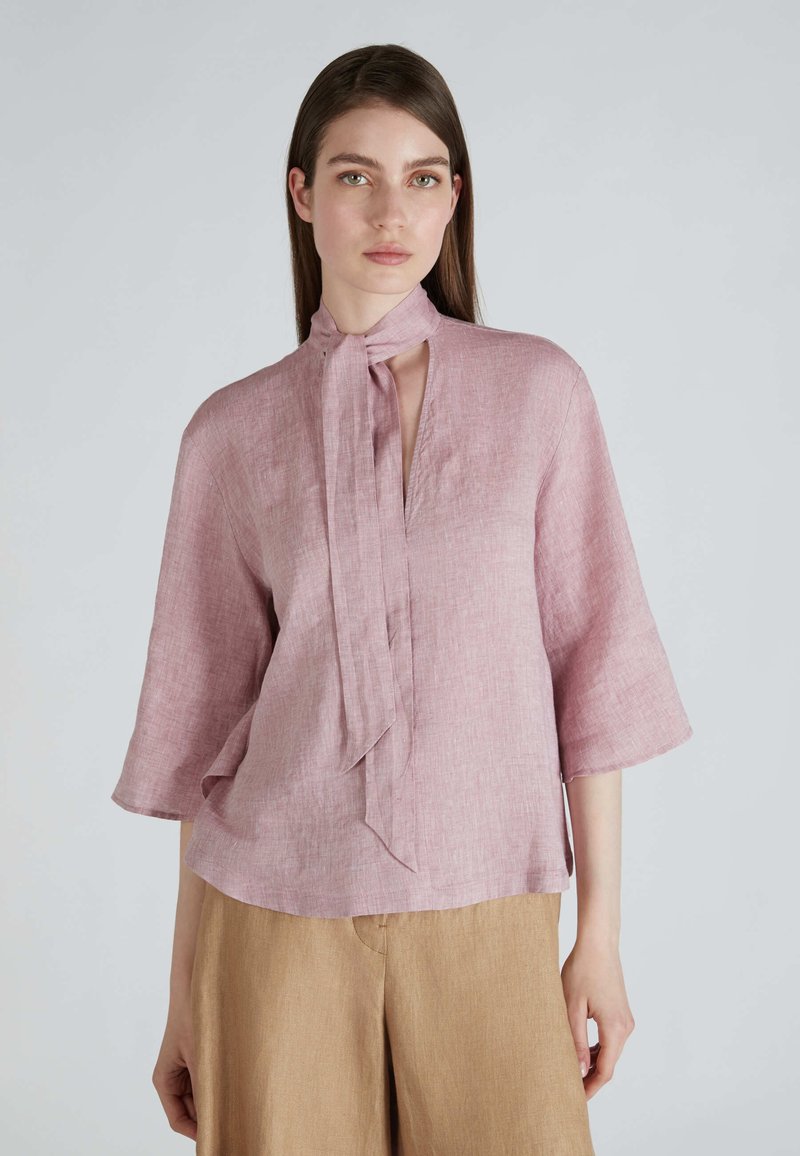 Blusa rosa chiaro in lino, caratterizzata da un colletto alto con nodo, maniche corte e una vestibilità morbida con una sottile texture.
