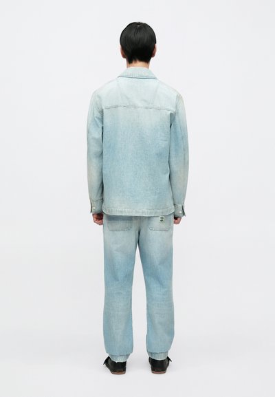 Ανοιχτό μπλε τζιν μπουφάν και τζιν παντελόνι σε χαλαρή γραμμή με διακριτική ξεθώριαση. Διαθέτει δύο πίσω τσέπες και λογότυπο στο παντελόνι.