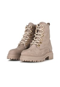 Bottines en suède beige avec un bout rond, une semelle épaisse et des œillets en métal. Dotées de lacets beiges et d'une finition texturée.