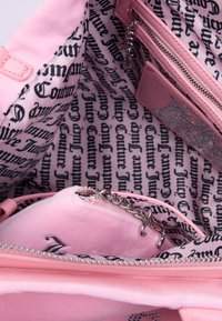 Borsa rosa con un'esterno liscio e una foderatura stampata con il testo "Juicy Couture". Include una tasca con zip e un interno morbido e soffice.
