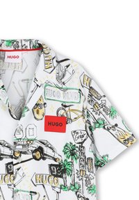 Korte mouw shirt met een witte achtergrond met kleurrijke schetsen van auto’s, borden en palmbomen. Rode logo patch op de borst.