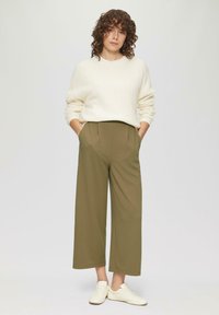 Crème kleurige geribde trui en olijfgroene wijde broek met plooien en zijzakken, in combinatie met witte sneakers op een neutrale achtergrond.