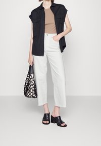 Camicia nera a maniche corte con bottoni, top avvitato color sabbia, jeans bianchi a gamba larga con orlo sfilacciato, mule neri con tacco a blocco, borsa a rete nera.