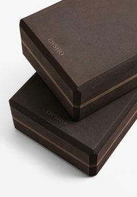 Tmavo hnedé obdĺžnikové škatule s matným povrchom, s tenkými vertikálnymi pruhmi a vyrazeným logom "OYSHO" na strane.