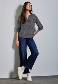 Svart- och vitmönstrad blus med V-ringning och långa ärmar, kombinerad med vida mörkblå jeans och vita sneakers.