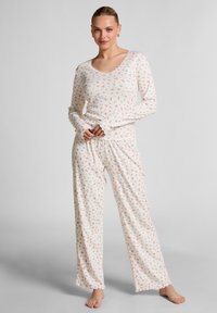 Long-sleeve pajama set in cream with a floral print, featuring a scalloped neckline and cuffs, soft fabric, and loose-fitting pants.