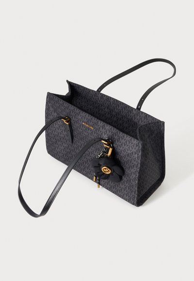 Черна чанта тип „тоут“ Michael Kors с повтарящ се лого мотив, дълги дръжки за рамо и декоративна висулка във формата на цвете със златисти акценти.