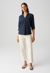 Camicia blu navy con collo a V e maniche a tre quarti, abbinata a pantaloni cropped color avorio e infradito neri. Texture liscia.