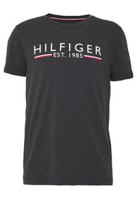 Camiseta de algodón gris con cuello redondo. Presenta el texto "HILFIGER EST. 1985" en blanco y rojo. Mangas cortas y un corte relajado.