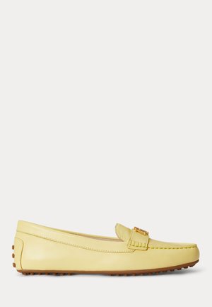 Κίτρινο μοκασίνι από δέρμα με καφέ λαστιχένια καρφιά στη σόλα και λεπτομέρεια με χρυσή αγκράφα στο μπροστινό μέρος.