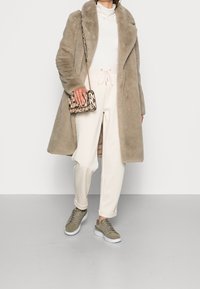 Beige faux pelsfrakke med brede revers, kombineret med en hvid ribstrikket sweater, cremefarvede joggingbukser og olivengrønne sneakers. Lille håndtaske med slangeprint.