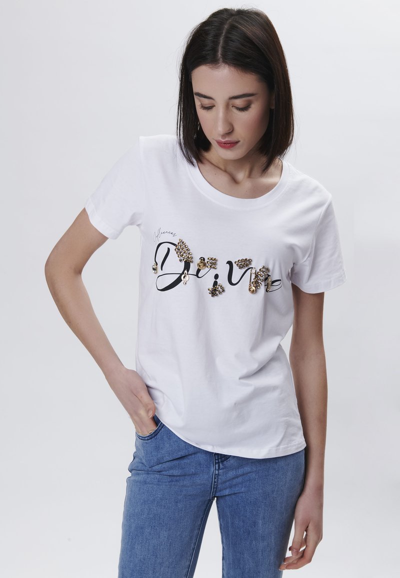 Camiseta blanca de algodón con texto negro en cursiva y detalles decorativos en dorado. Mangas cortas y escote redondo. Corte casual.