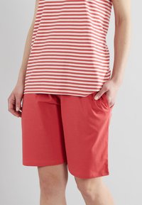 Haut sans manches rayé rouge associé à un short rouge uni. Les deux sont en tissu doux ; le short comporte une taille élastique et une coupe ample.