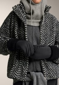 Jachetă cu un model herringbone în nuanțe de negru și gri, cu guler înalt, asortată cu un pulover gri cu dungi și mănuși negre căptușite. Materiale texturate observate.