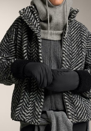 Sako s čierno-sivým vzorom rybej kosti a vysokým golierom, spárované so šedým rebrovaným sveterom a čiernymi vypodšívkovanými rukavicami. Zaznamenané textúrované materiály.