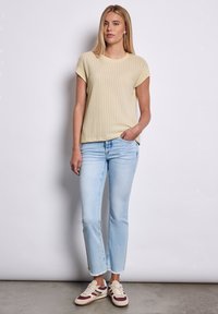 Světle žlutý žebrovaný top s krátkým rukávem spárovaný se světle modrými zkrácenými džíny a multibarevnými teniskami; uvolněný silueta, měkká textura.